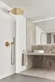 Moderne Badezimmeransicht mit goldenen Armaturen von Ideal Standard. Die Dusche ist durch eine Glaswand abgetrennt, mit einer schlichten weißen Waschschüssel und einem Handtuchhalter.